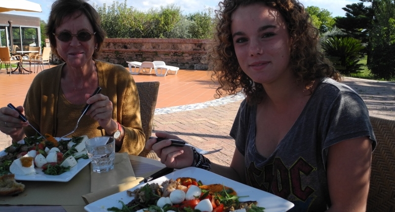 Woman visitor and young girl in front of two big plates with mozzarella cheese and fresh vegetables outdoors in the mozzarella chees farm terrace